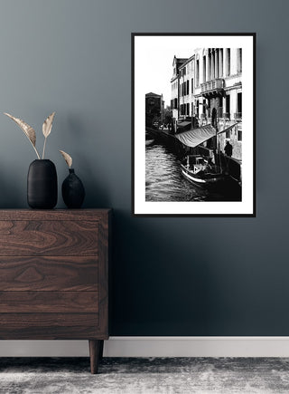 Black and white poster of a boat on a Venice canal, displayed above a wooden dresser in a modern room.