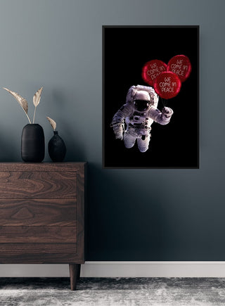 Poster of an astronaut floating with red balloons that say "We come in peace," displayed above a dark wooden dresser.
