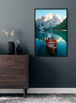 Framed poster of an astronaut in a canoe on a serene lake with mountains, displayed above a wooden dresser.