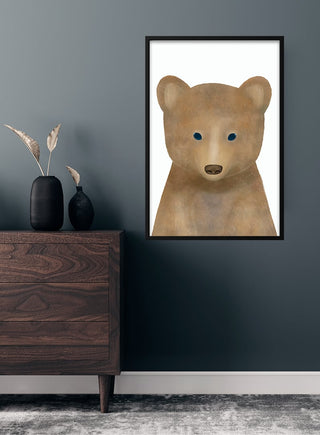 Framed poster of a cute brown bear with blue eyes, displayed above a dresser in a child's room.