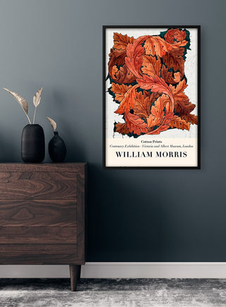 Framed William Morris Acanthus Plakat with bold red and orange acanthus leaves, hanging on a dark wall above a dresser.