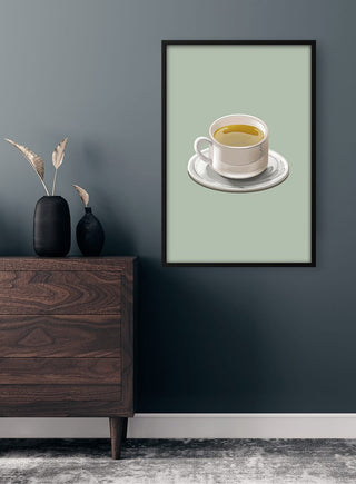 A framed Green Tea Plakat featuring a cup of green tea hangs on a dark wall above a wooden dresser.