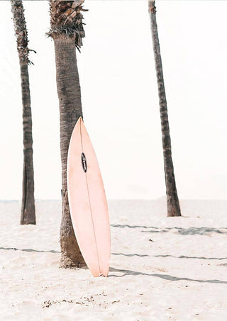 A pink surfboard rests against a palm tree on a sandy beach, with clear sky in the background.