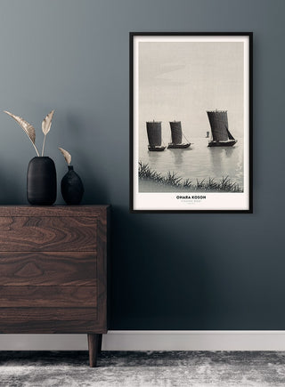 Framed Ohara Koson Fishing Boat Plakat on a dark wall above a dresser with vases and pampas grass.