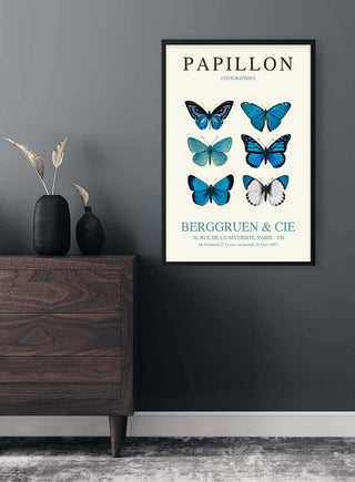 Framed Blue Papillon Plakat featuring illustrations of blue butterflies, displayed above a wooden dresser.