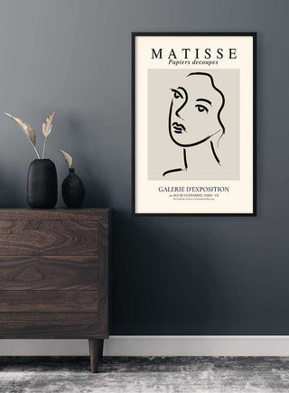 Minimalist line art of a woman's face in Matisse style, framed and hanging above a wooden dresser.