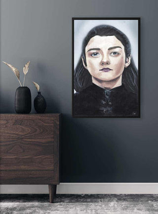 Framed portrait of Arya Stark titled "The Gorgeous Girl" hanging on a dark gray wall above a wooden dresser.