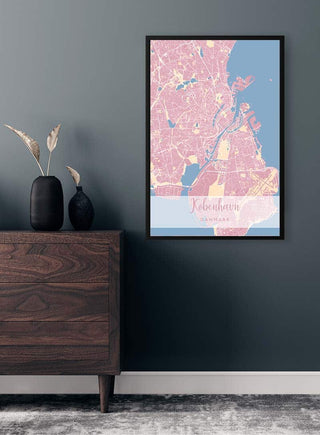 Framed København By Plakat Lyserød map poster hanging on a gray wall above a wooden dresser with vases.