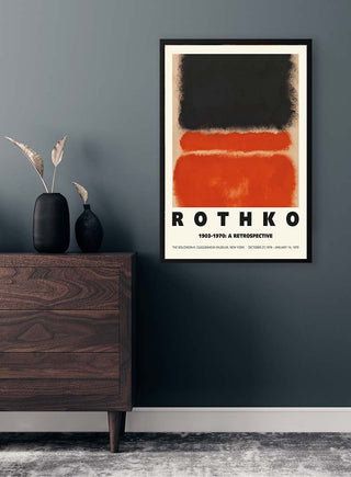 A framed Mark Rothko retrospective poster with abstract shapes hangs on a dark wall above a wooden dresser.