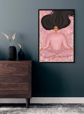Framed artwork of a meditative woman in pink, displayed on a dark wall above a wooden dresser.