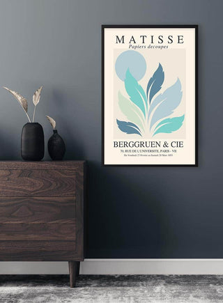 Framed "Matisse Inspired Blue Sun" art print with abstract blue leaves on a grey wall above a wooden dresser.