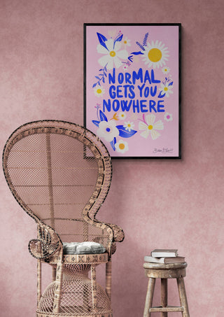 Framed "Normal Gets You Nowhere" wall art with floral design displayed above a wicker chair and stool.