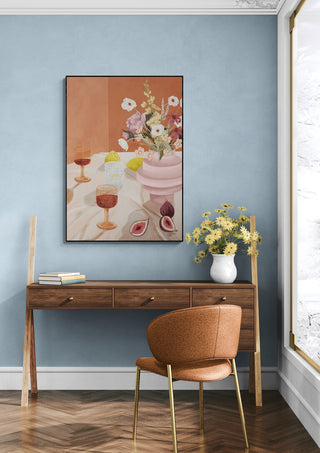 Framed "Summer Stories - Goed Blauw" art print above a wooden desk with flowers in a vase, in a modern room.