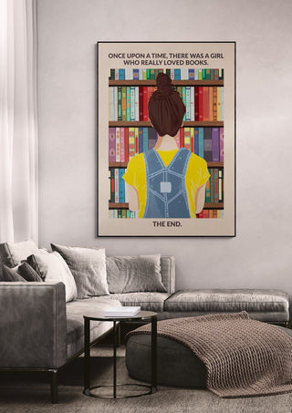 Framed Book Girl wallchart featuring a girl in overalls facing a colorful bookshelf, displayed above a sofa.
