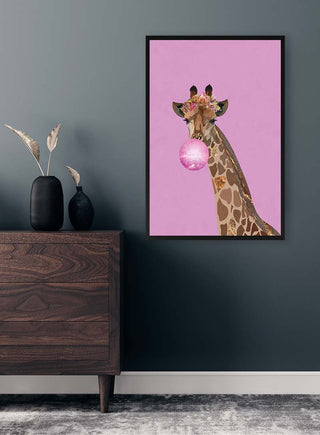 Framed art of a giraffe blowing pink bubblegum with flowers on its head, displayed in a modern room.