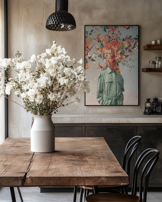 Framed "You Smell Like Home - Frank Moth" art on wall above rustic table with white flowers in vase.