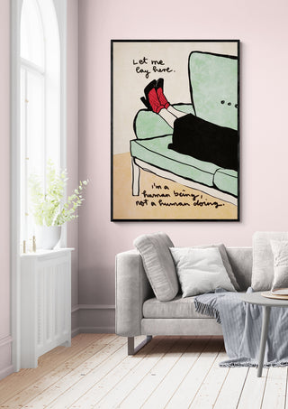 Framed "Let me lay here" artwork by Raissa Oltmanns displayed on a pink wall above a modern sofa.