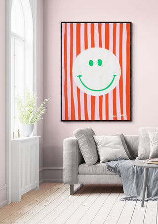 Framed Pink Smiley In Stripes - Baroo Bloom artwork hanging on a light pink wall above a gray sofa in a bright room.