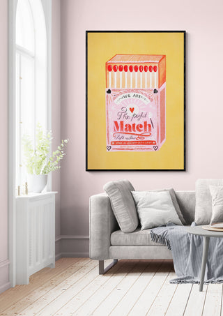 Framed print of "The Perfect Match" matchbox artwork hangs on a pink wall above a grey sofa.