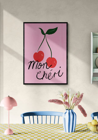 Framed Mon Cheri Cherry artwork with two cherries, displayed above a dining table in a bright room.