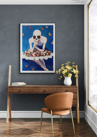 Framed Trumpster by Martin Zen artwork hanging above a wooden desk with a vase of yellow flowers.