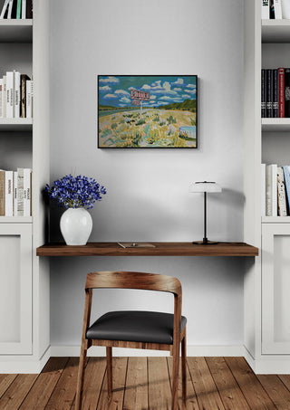 Meet Me At The Motel by Eleanor Baker hanging above a home desk setup with bookshelves and a vase of flowers.