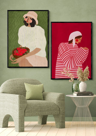 Two framed artworks, including The Woman With the Red Stripes by Bea Muller, displayed on a green wall above a chair.