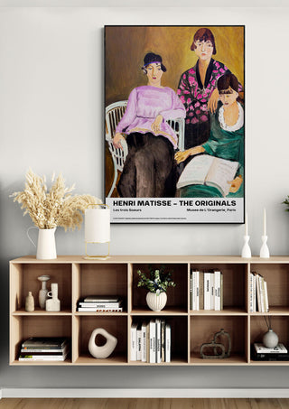 Framed "Les Trois Soeurs" by Henri Matisse displayed above a modern wooden shelf with books and decor.